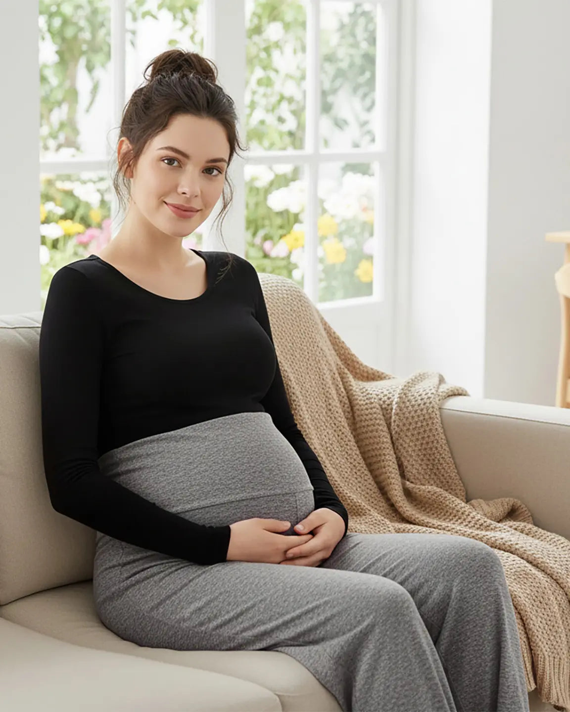 Pregnant woman in black long-sleeve top and gray wide-leg maternity pants with over-belly waistband.