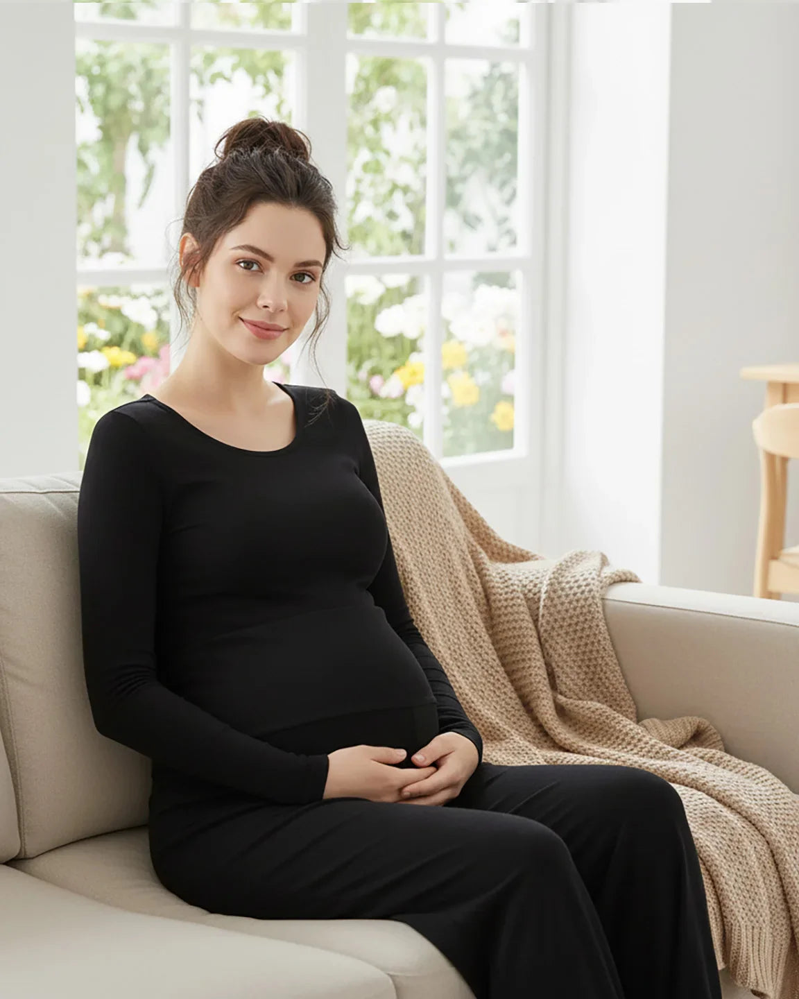 Pregnant woman in black long-sleeve top and relaxed wide-leg maternity pants, sitting on a sofa.