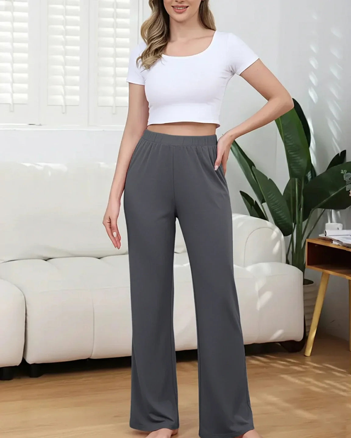Woman wearing dark gray stretch flared maternity pants with pockets and a white crop top.