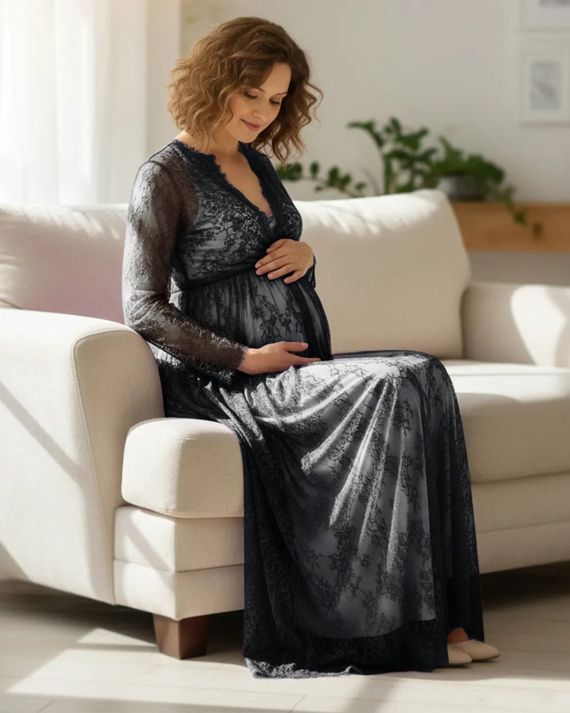 Pregnant woman in a black sheer floral lace empire waist maternity maxi dress, gently holding her belly.