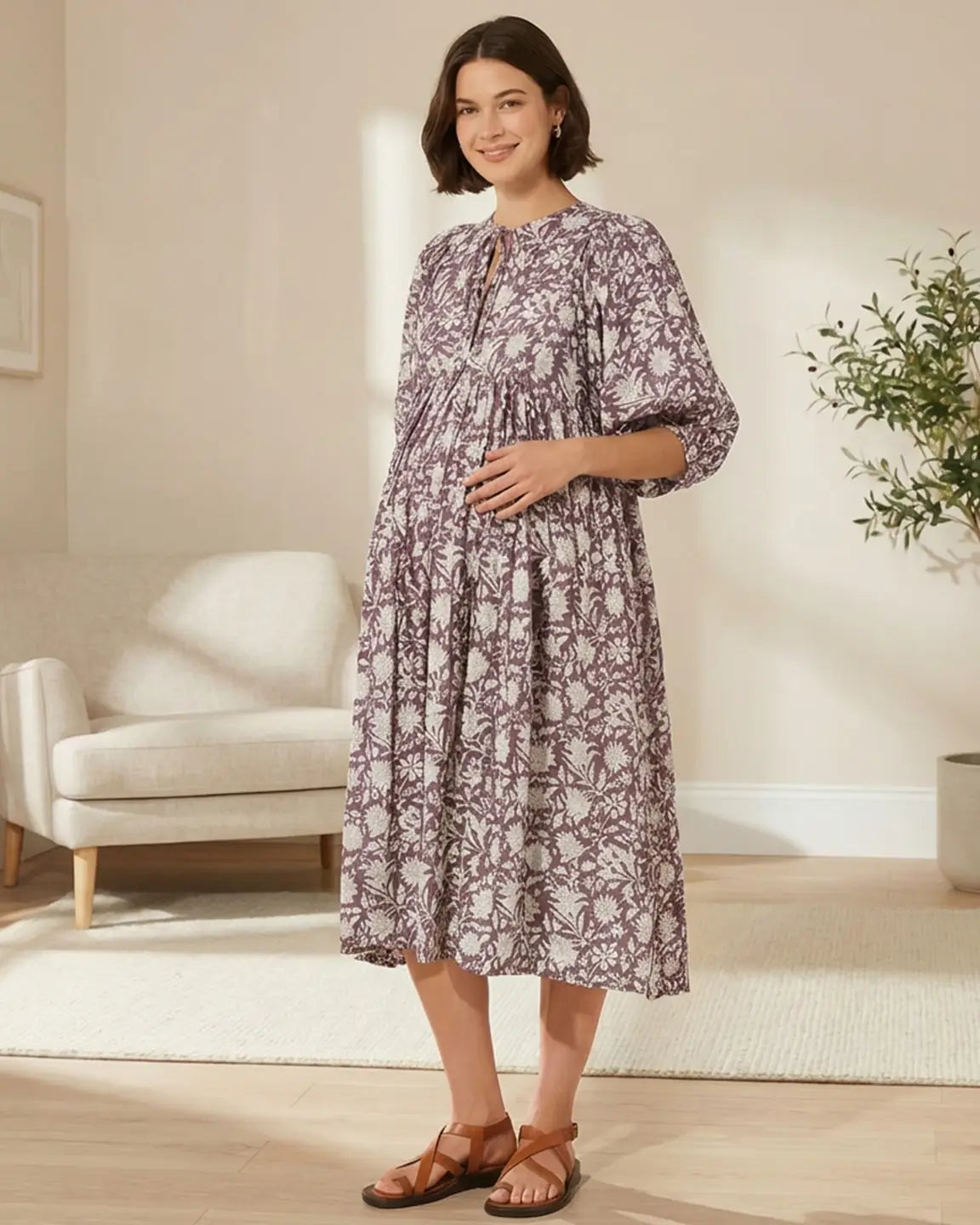 Smiling pregnant woman in a loose-fit purple and white floral maternity midi dress with gathered shoulders.