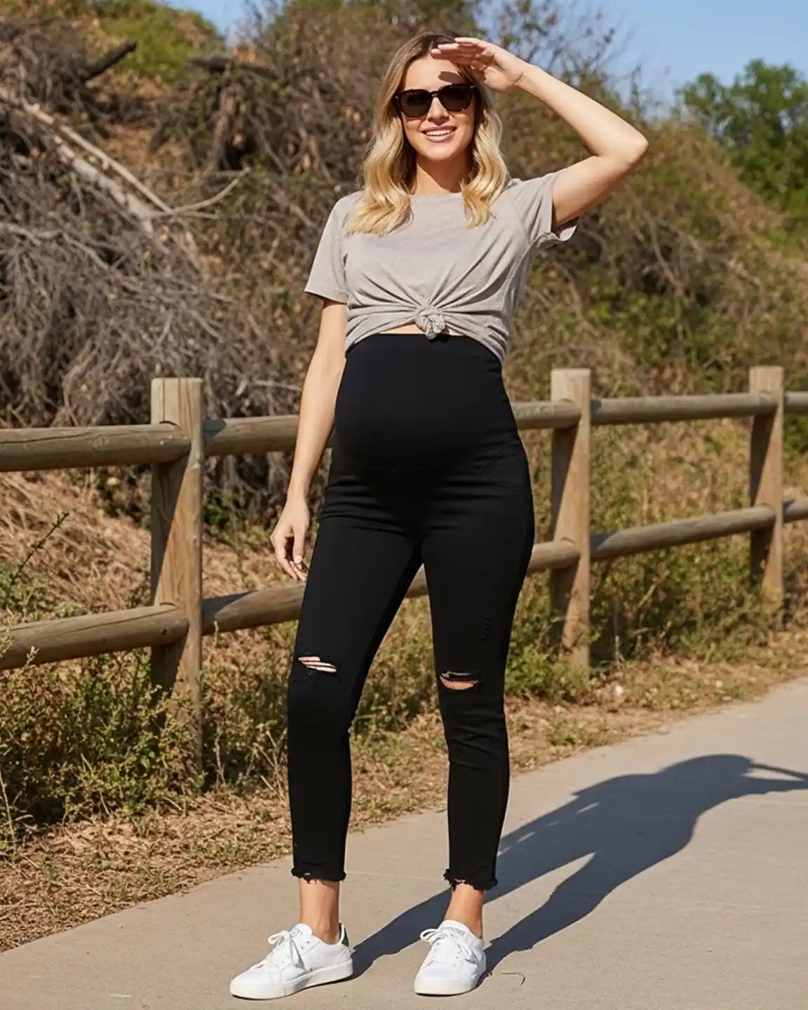 Smiling pregnant woman in black ripped maternity skinny jeans with an over-belly panel and frayed ankles.