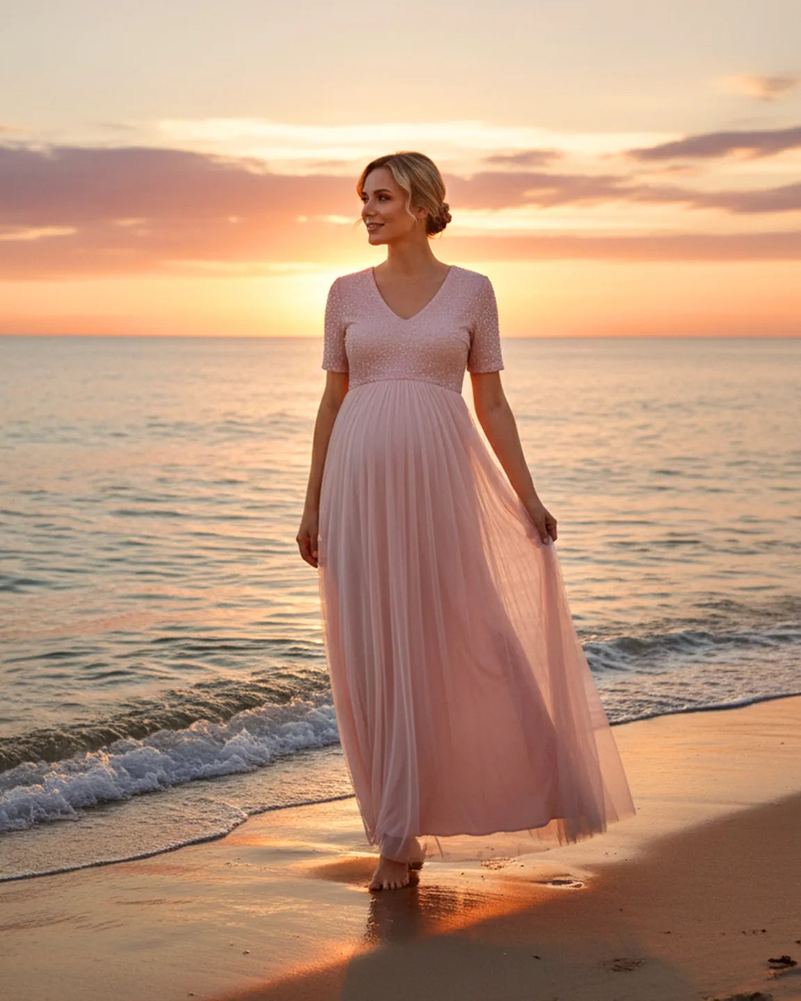 Pink sequin A-line maternity gown with V-neck and short sleeves, worn by a pregnant woman on a beach at sunset.
