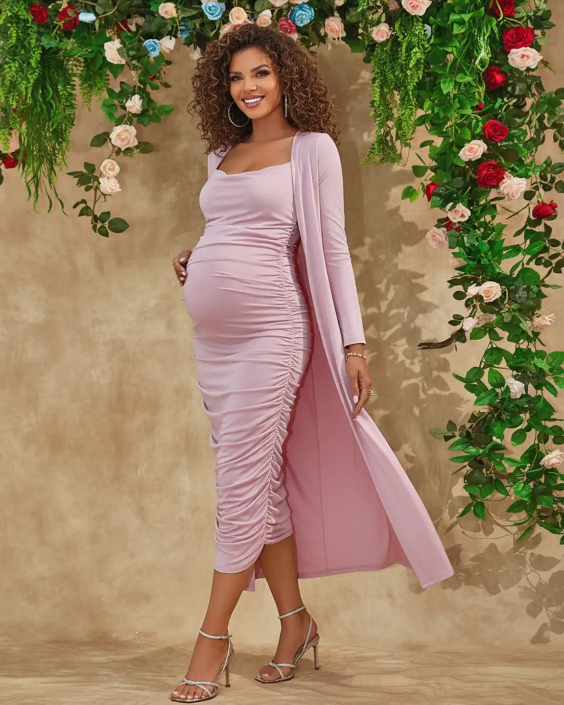 Smiling pregnant woman in a pink side-ruched maternity slip dress and long-sleeve cardigan set.