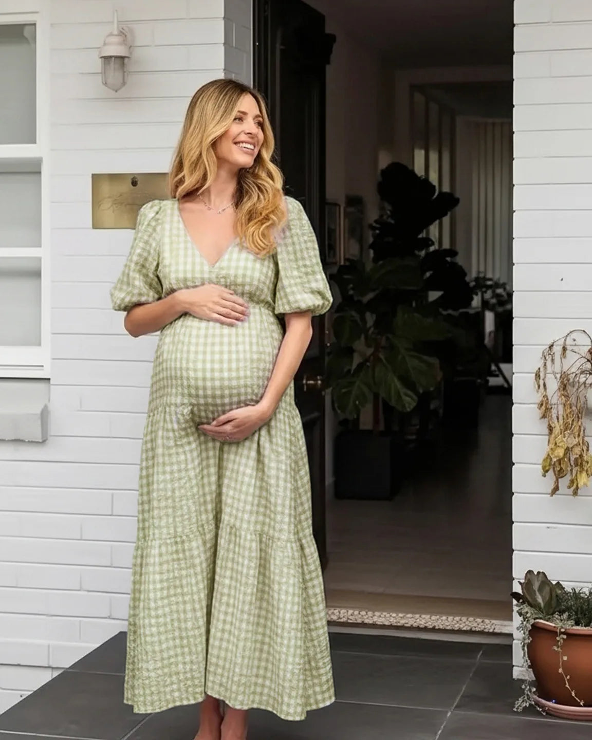 Pregnant woman in a green checkered maternity maxi dress with puffed sleeves, smiling outdoors.