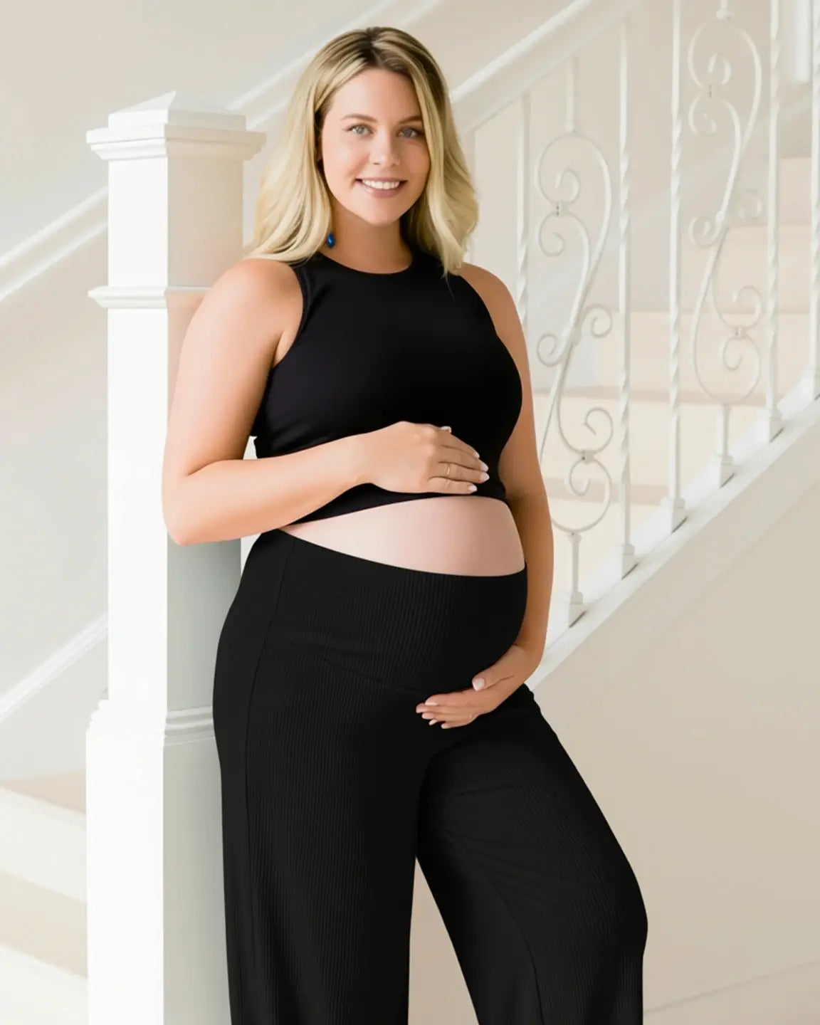 Smiling pregnant woman in black ribbed wide-leg maternity pants with over-bump waistband and black crop top.