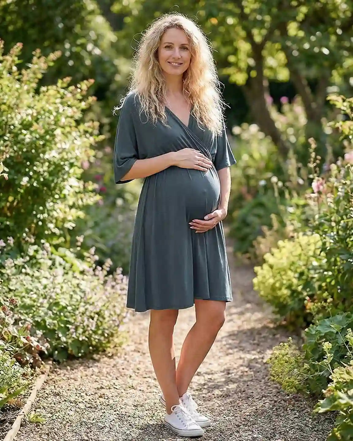 Pregnant woman in a charcoal gray cross-front maternity midi dress with 3/4 sleeves, standing in a garden.
