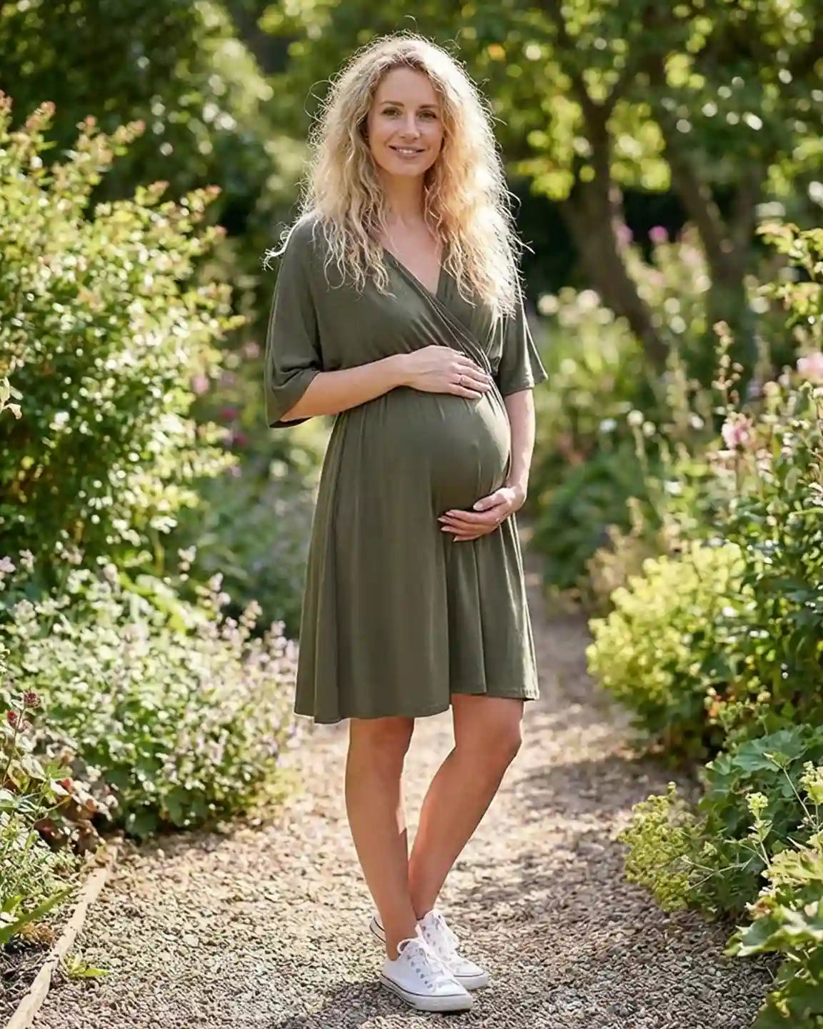 Pregnant woman in a green cross-front maternity midi dress, with 3/4 sleeves, in a garden.