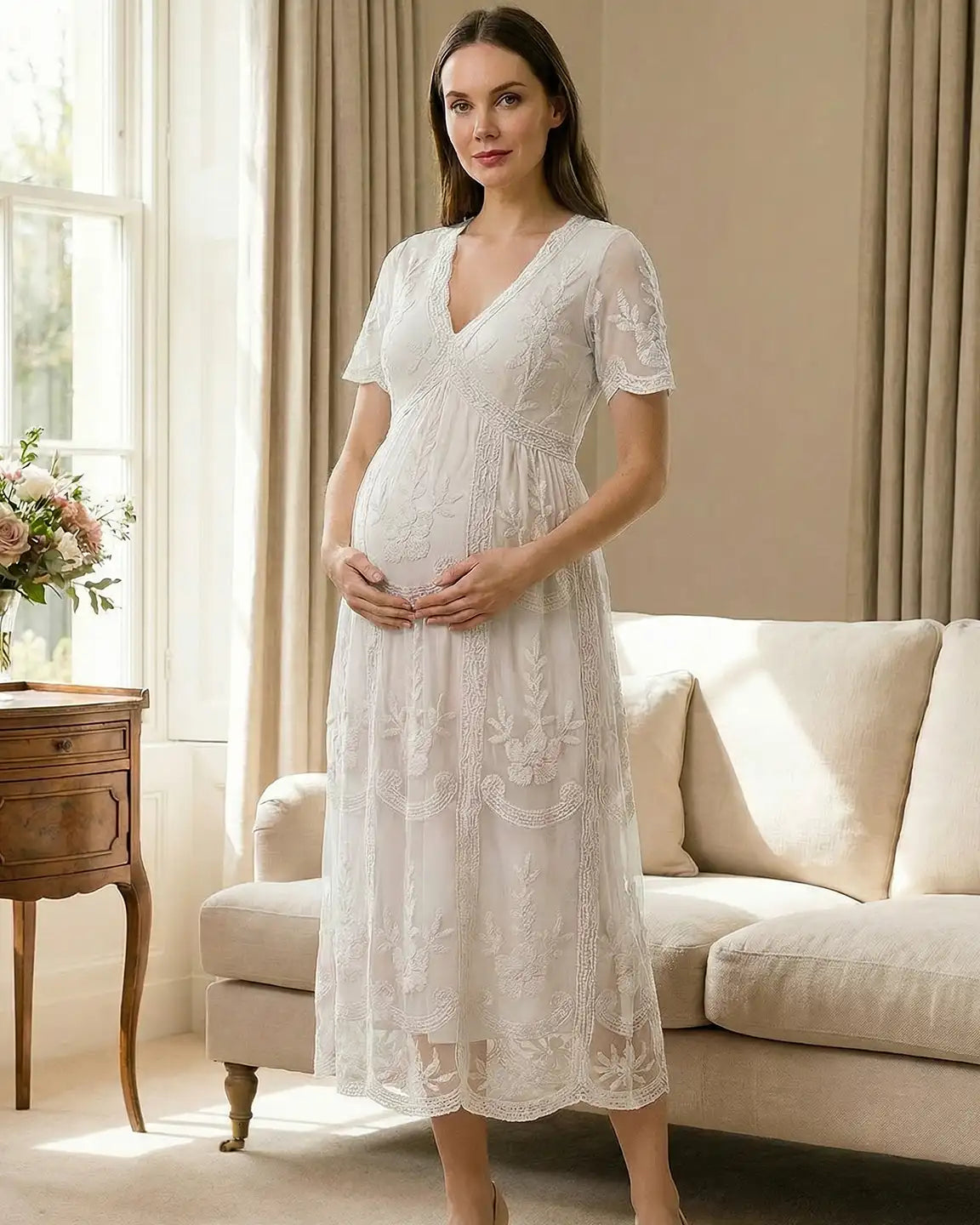 Pregnant woman in a white lace maternity midi dress with V-neck, short sleeves, and intricate embroidery.