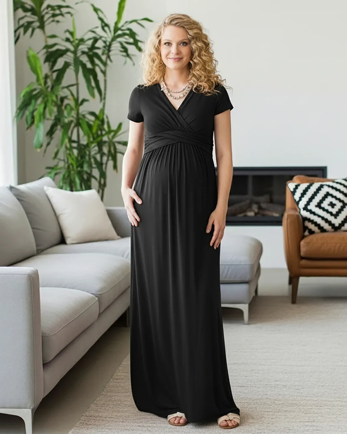 Woman in a black, short-sleeve, twist-front draped maternity nursing maxi dress, smiling.