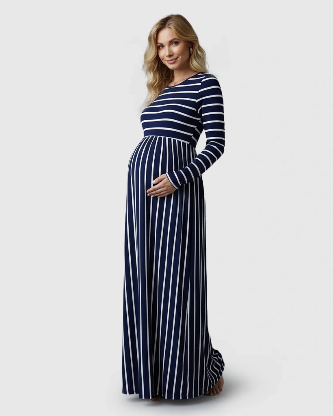 Blonde pregnant woman in a navy and white striped long sleeve maternity maxi dress, holding her bump.