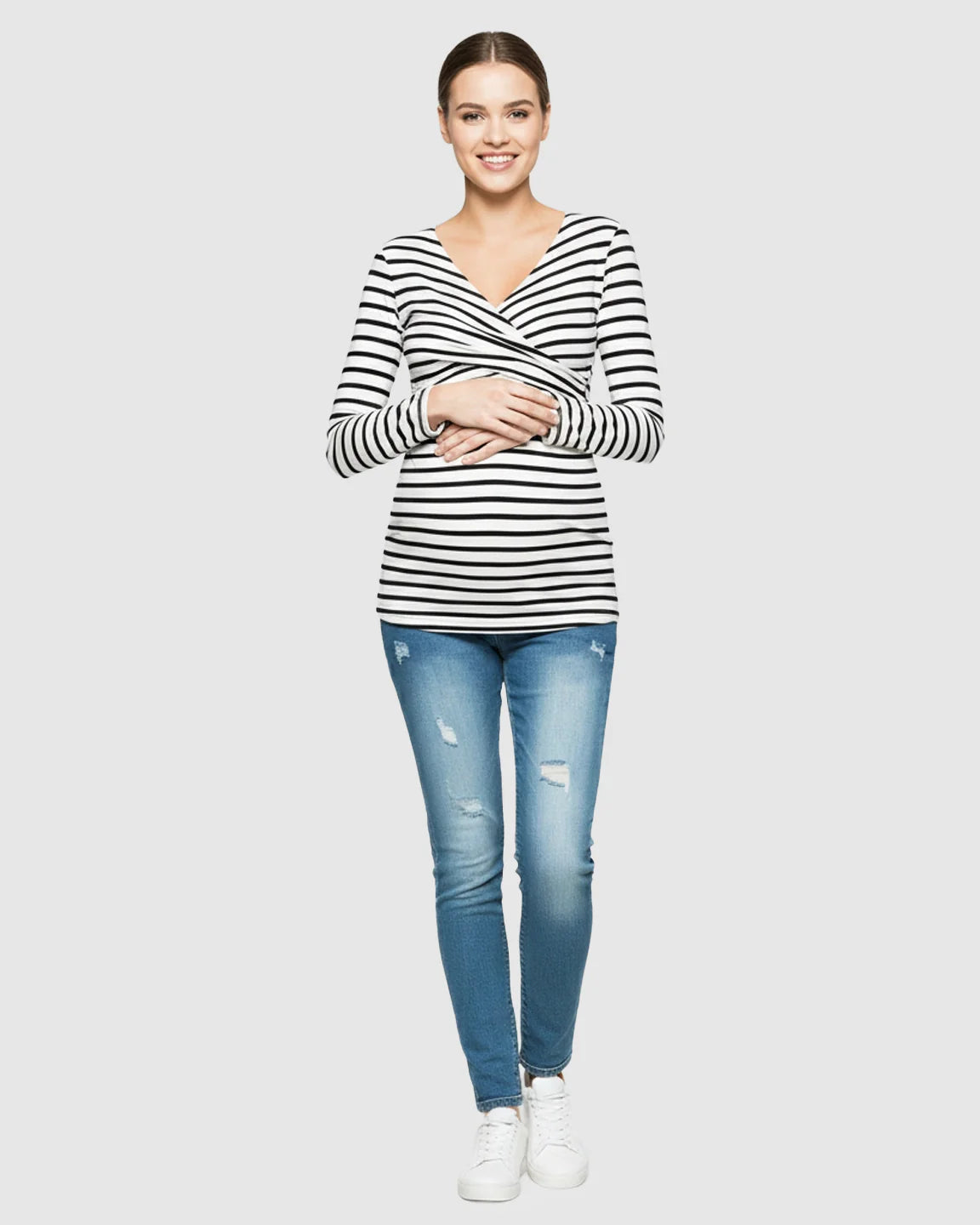Smiling woman in a black and white striped long-sleeve V-neck maternity and nursing top with distressed jeans.