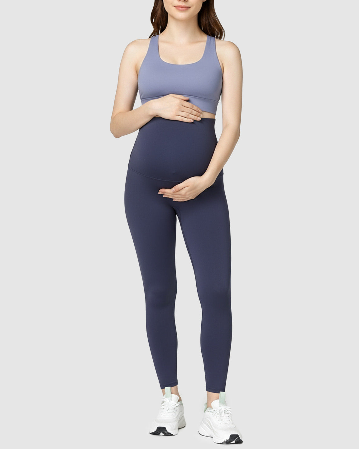Woman wearing navy high-waist soft stretch maternity leggings and a periwinkle sports bra.