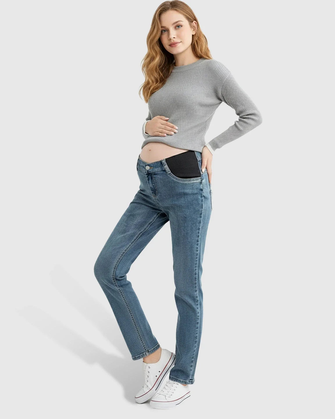 Woman in blue straight-leg maternity jeans with black side panels, a grey ribbed sweater, and white sneakers.