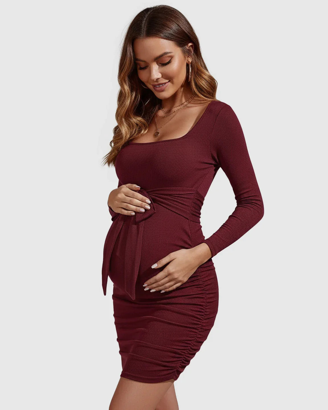 Pregnant woman in a burgundy ribbed bodycon maternity dress with square neckline, long sleeves, tie-waist, and side ruching.