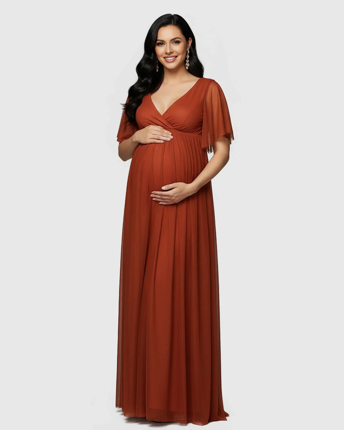 Smiling pregnant woman in a rust V-neck chiffon empire waist maternity maxi dress with flutter sleeves.