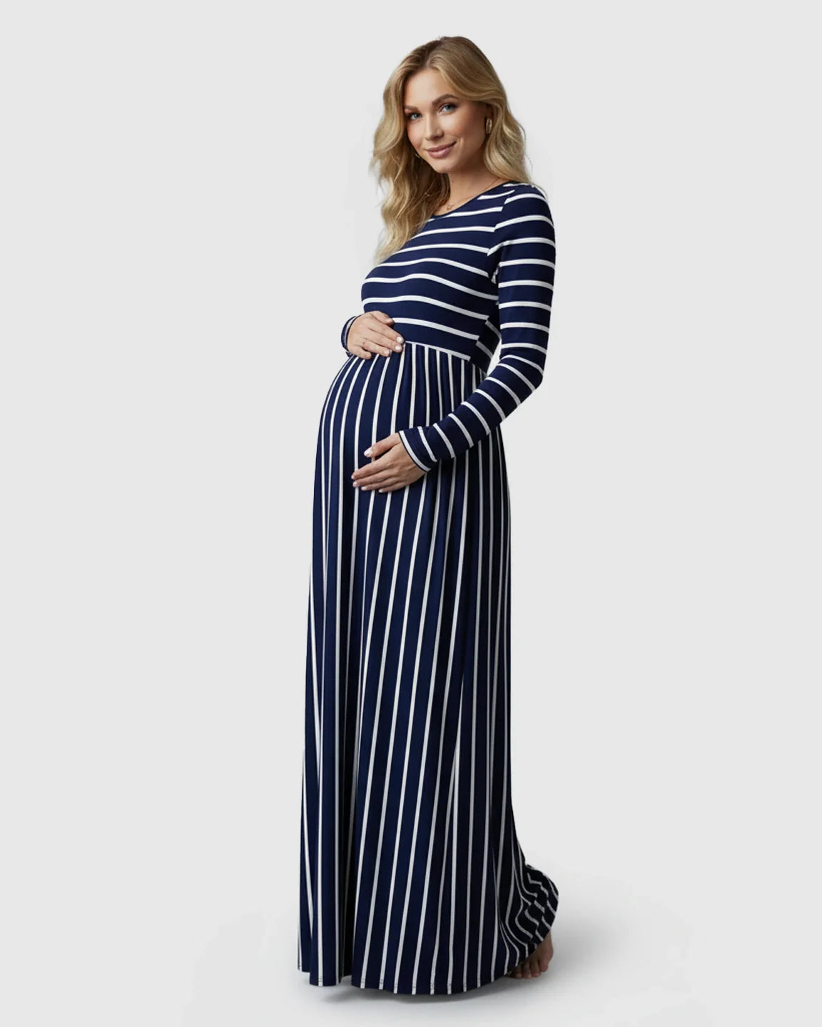 Pregnant woman in a navy and white striped long sleeve maternity maxi dress, hands on belly.