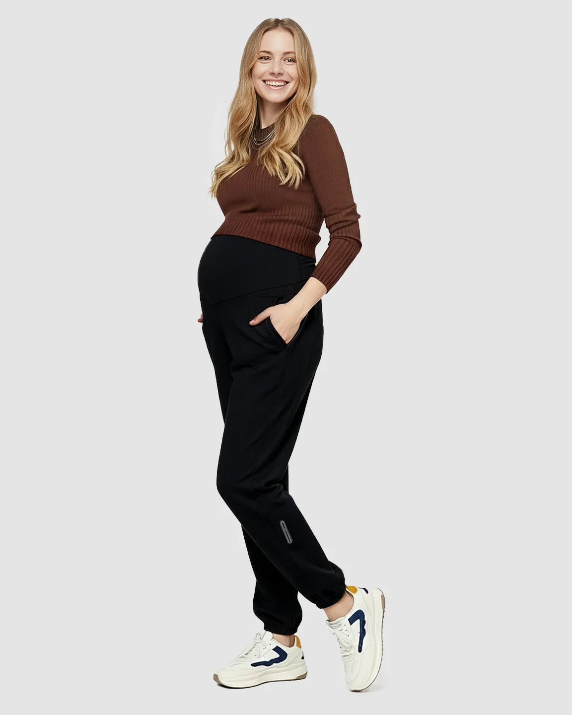 Smiling pregnant woman in black soft knit maternity joggers with pockets and a brown top.