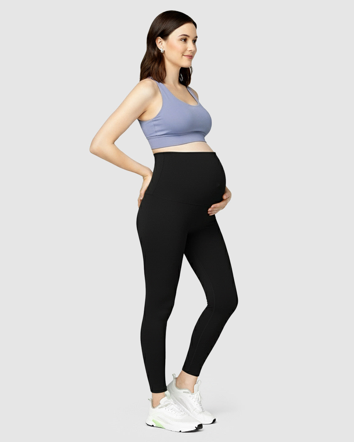 Smiling pregnant woman in black high-waist maternity leggings and a periwinkle sports bra.