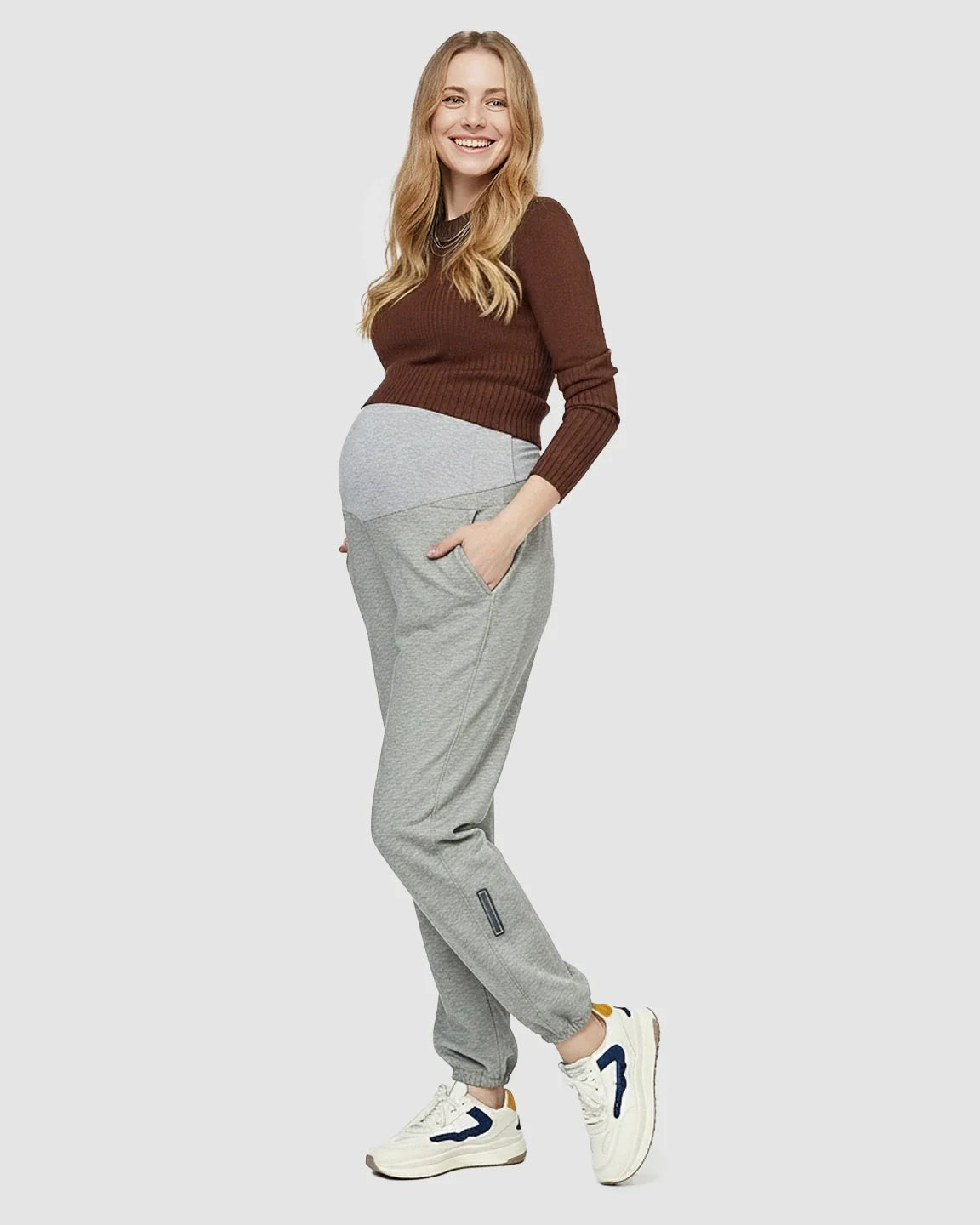 Smiling pregnant woman in gray soft knit maternity joggers with pockets and a brown top.