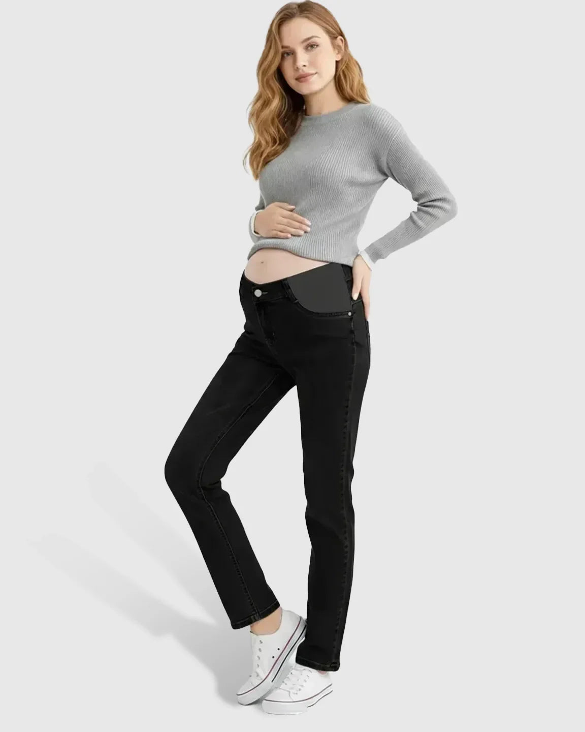 Woman in black straight-leg maternity jeans with side panels, a grey sweater, and white sneakers.