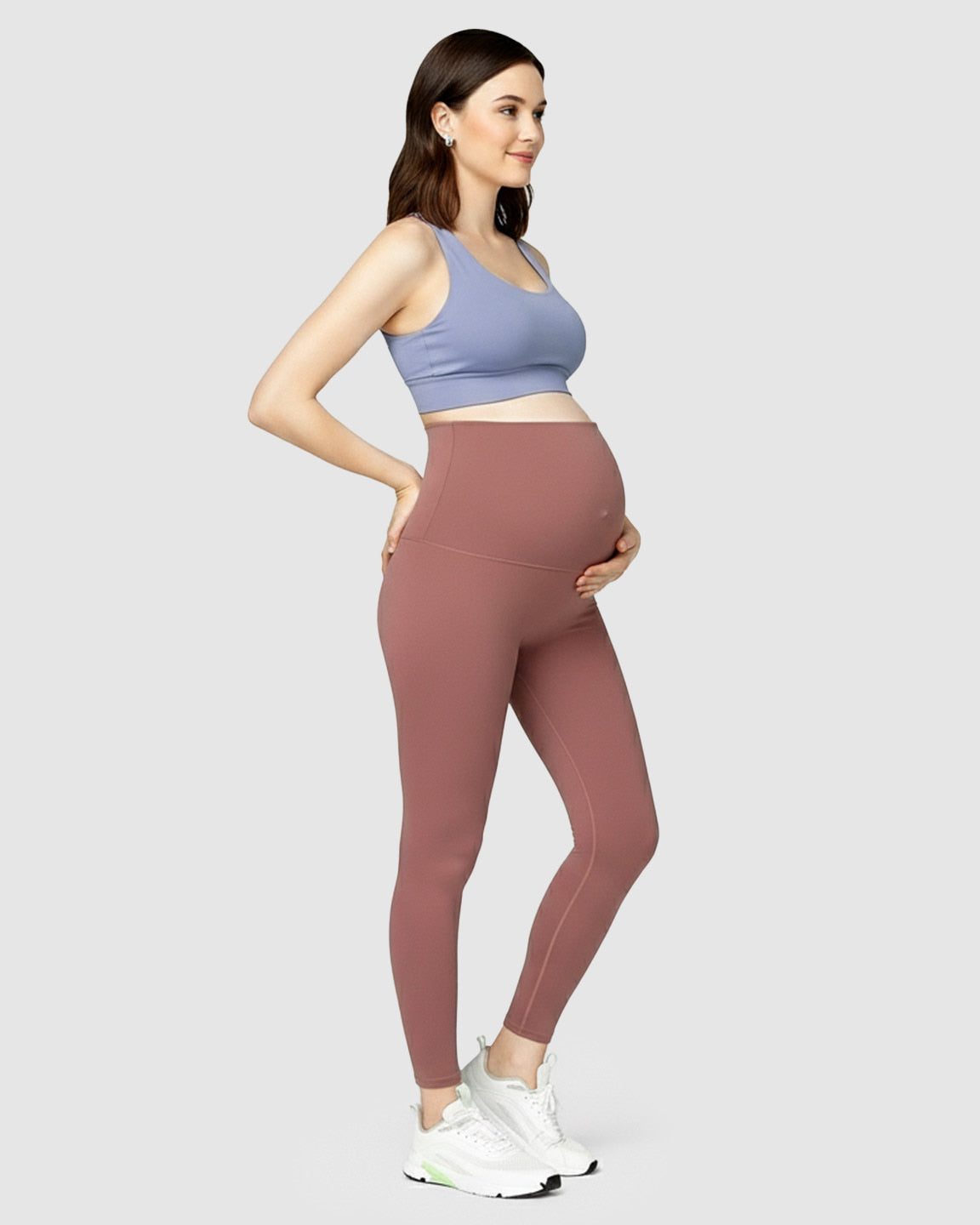 Pregnant woman smiling, wearing high-waist rose-colored soft stretch maternity leggings and a blue sports bra.