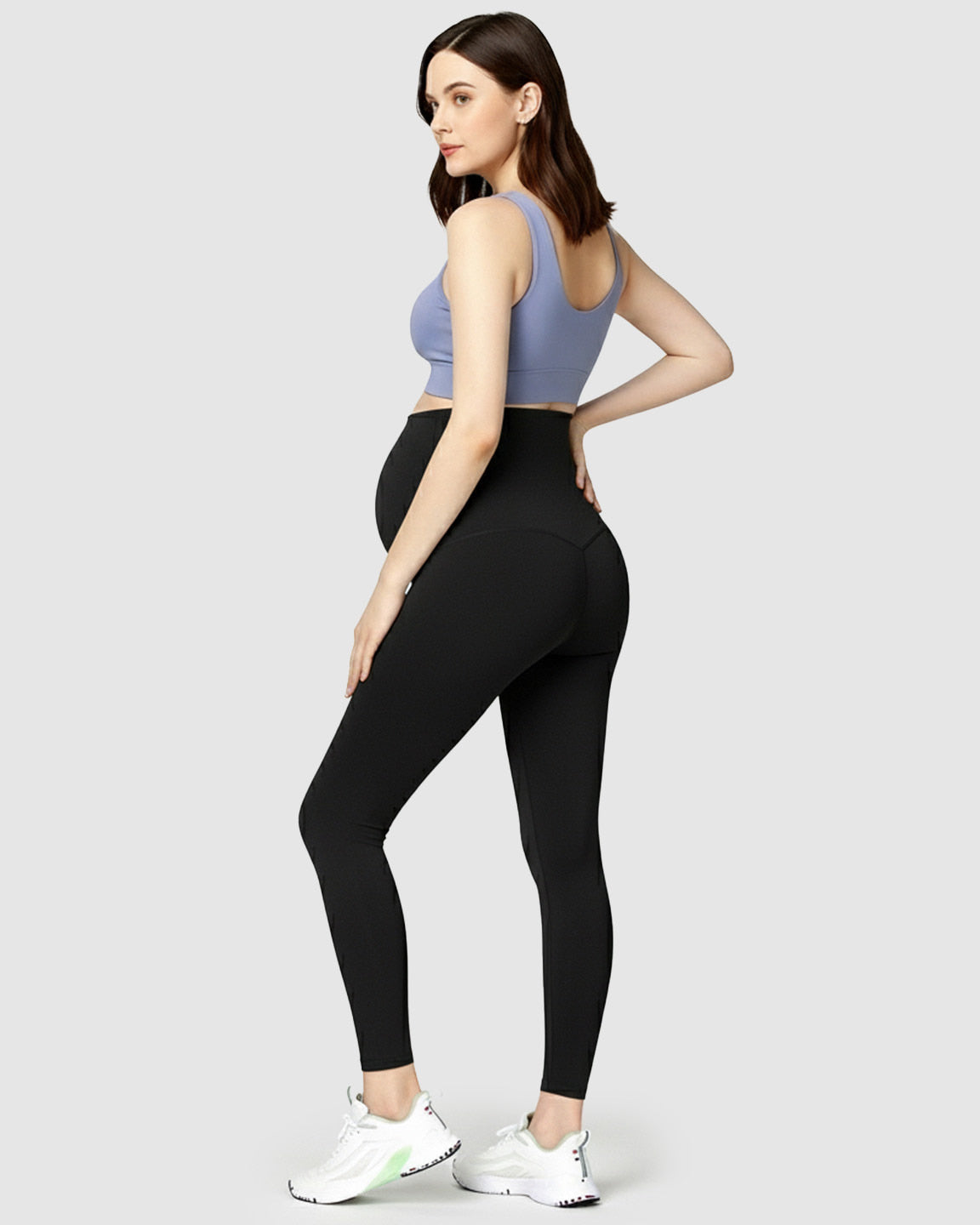 Woman wearing black high-waist maternity leggings and a periwinkle sports bra, showcasing bump support.