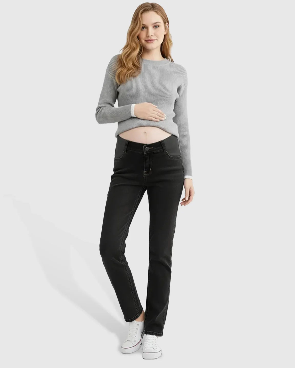 Woman wearing black straight-leg maternity jeans with side panels and a grey ribbed sweater, gently holding her belly.