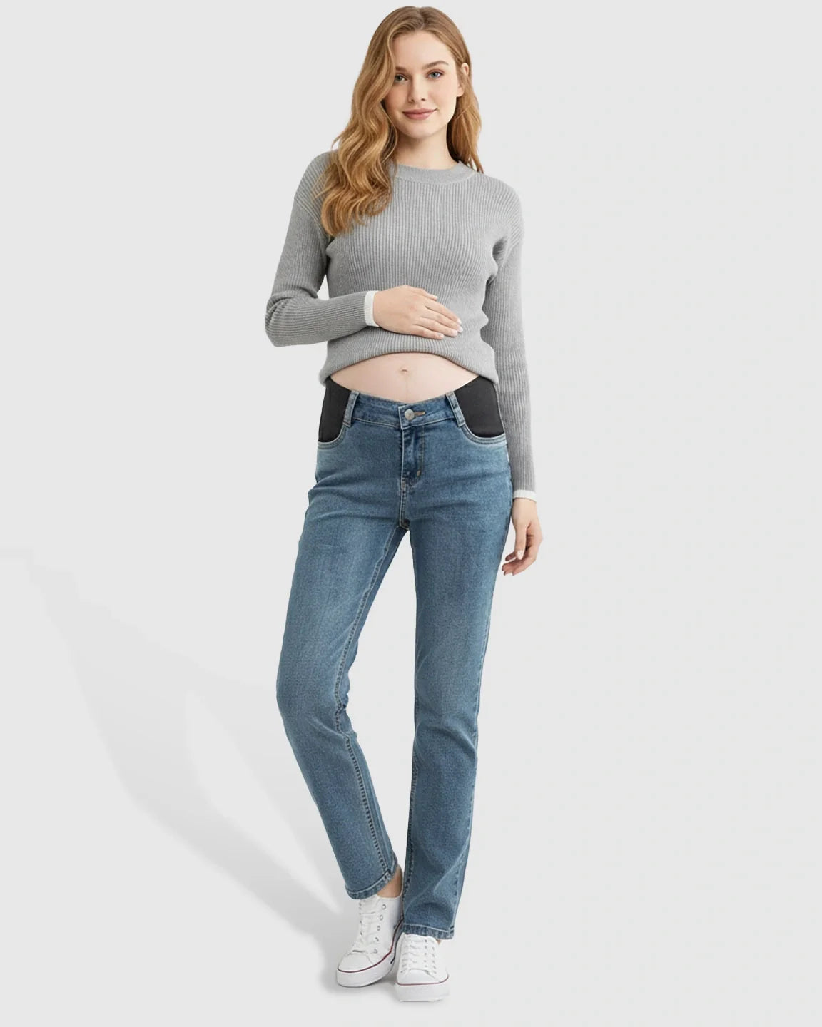 Smiling pregnant woman in blue straight-leg maternity jeans with black side panels and a grey ribbed sweater.