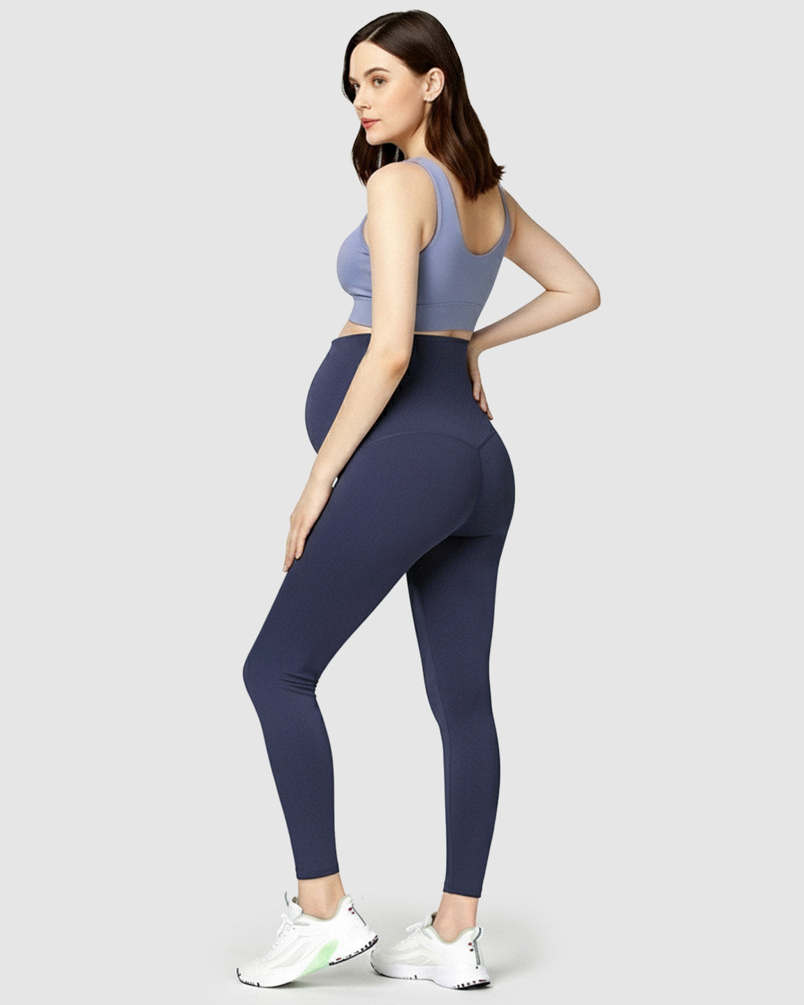 Pregnant woman wearing navy high-waist soft stretch maternity leggings and a periwinkle sports bra.