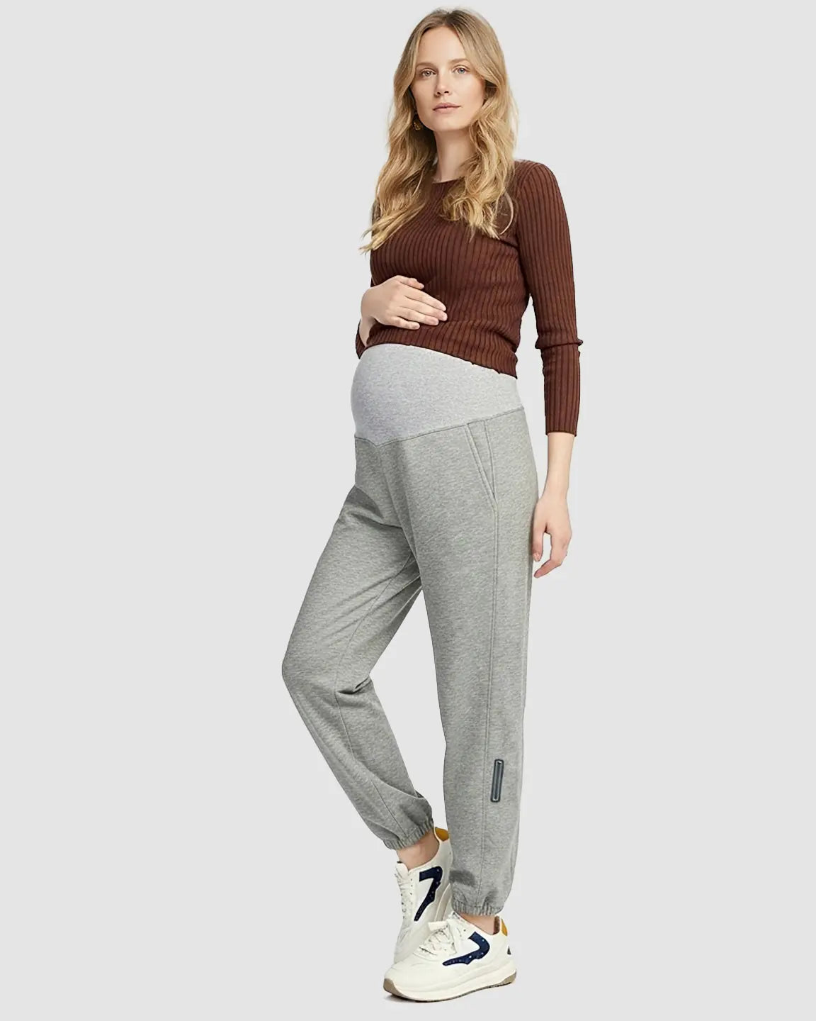 Pregnant woman in grey soft knit maternity joggers with a light grey supportive waistband and side pockets.