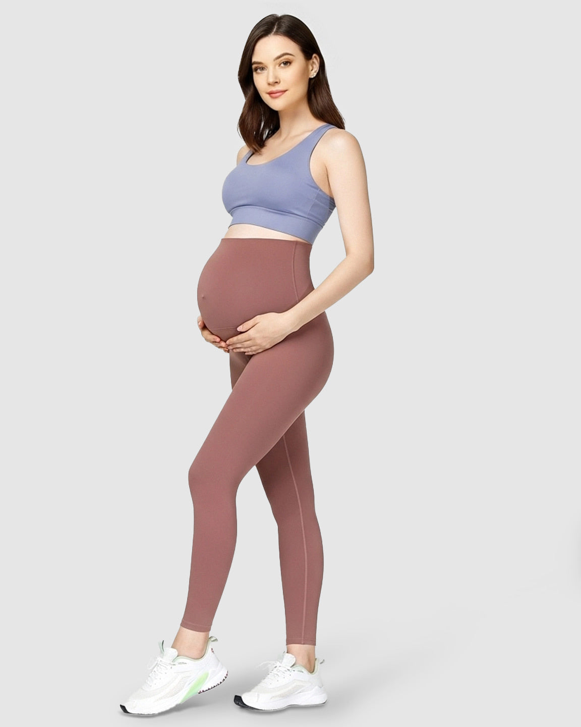 Pregnant woman in rose brown high-waist soft stretch maternity leggings and a blue sports bra.