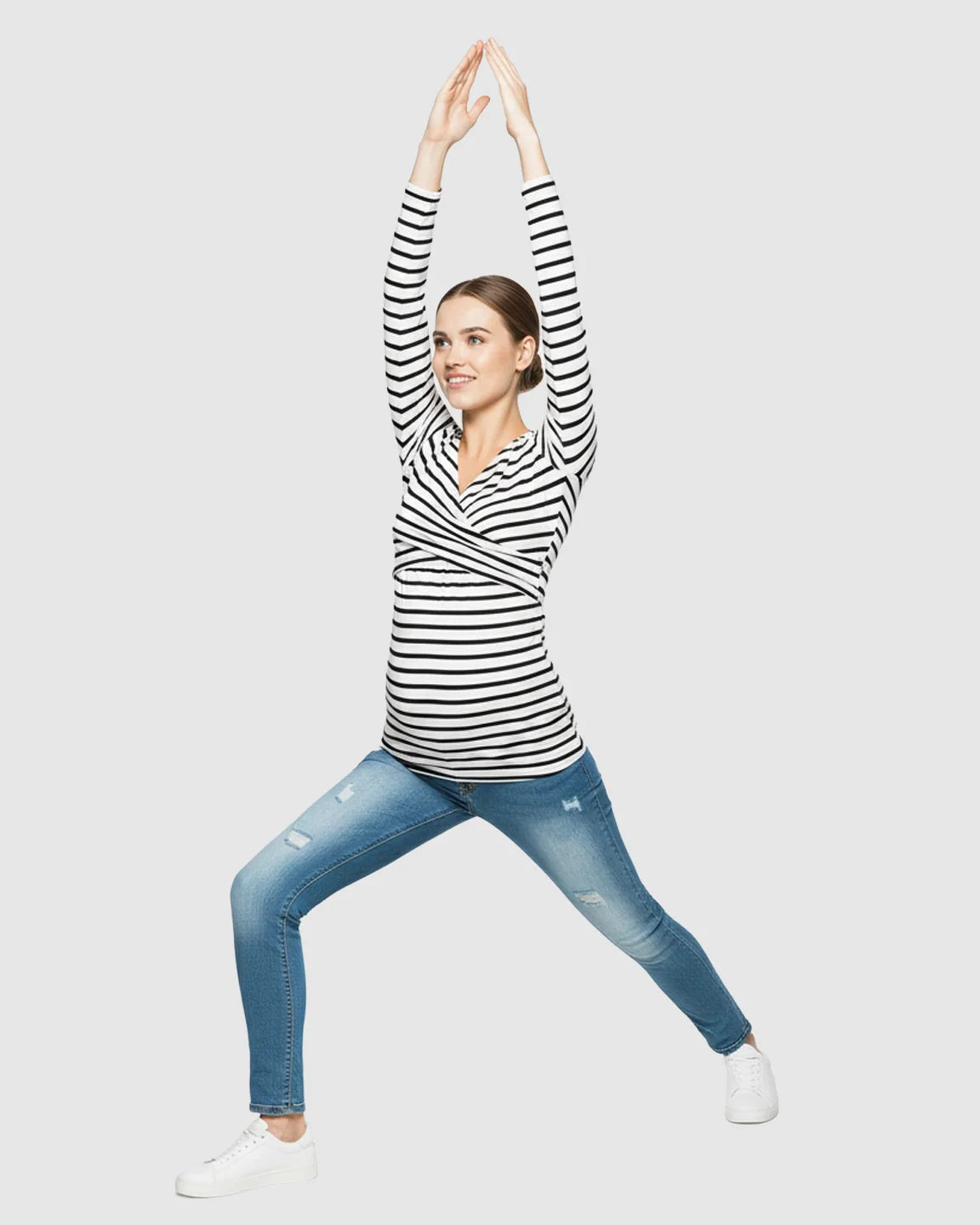 Pregnant woman in a black and white striped long-sleeve V-neck maternity shirt and jeans, arms raised.