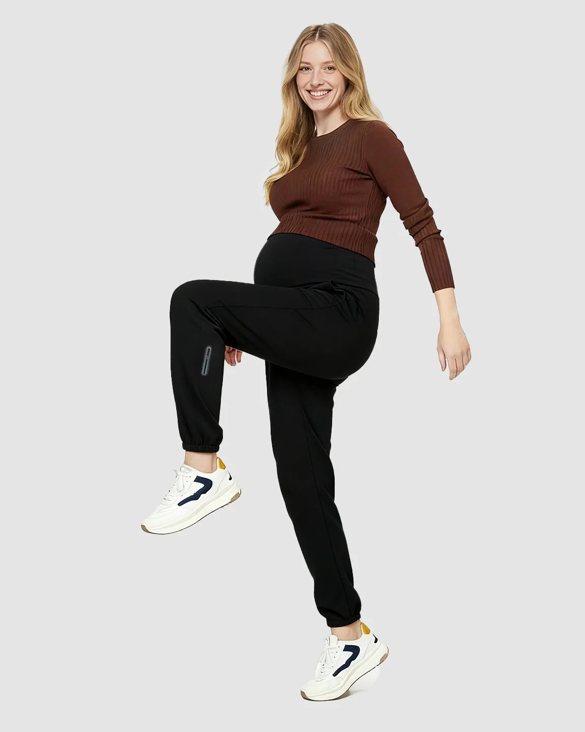 Smiling pregnant woman in black soft knit maternity joggers with side pockets and a brown top.