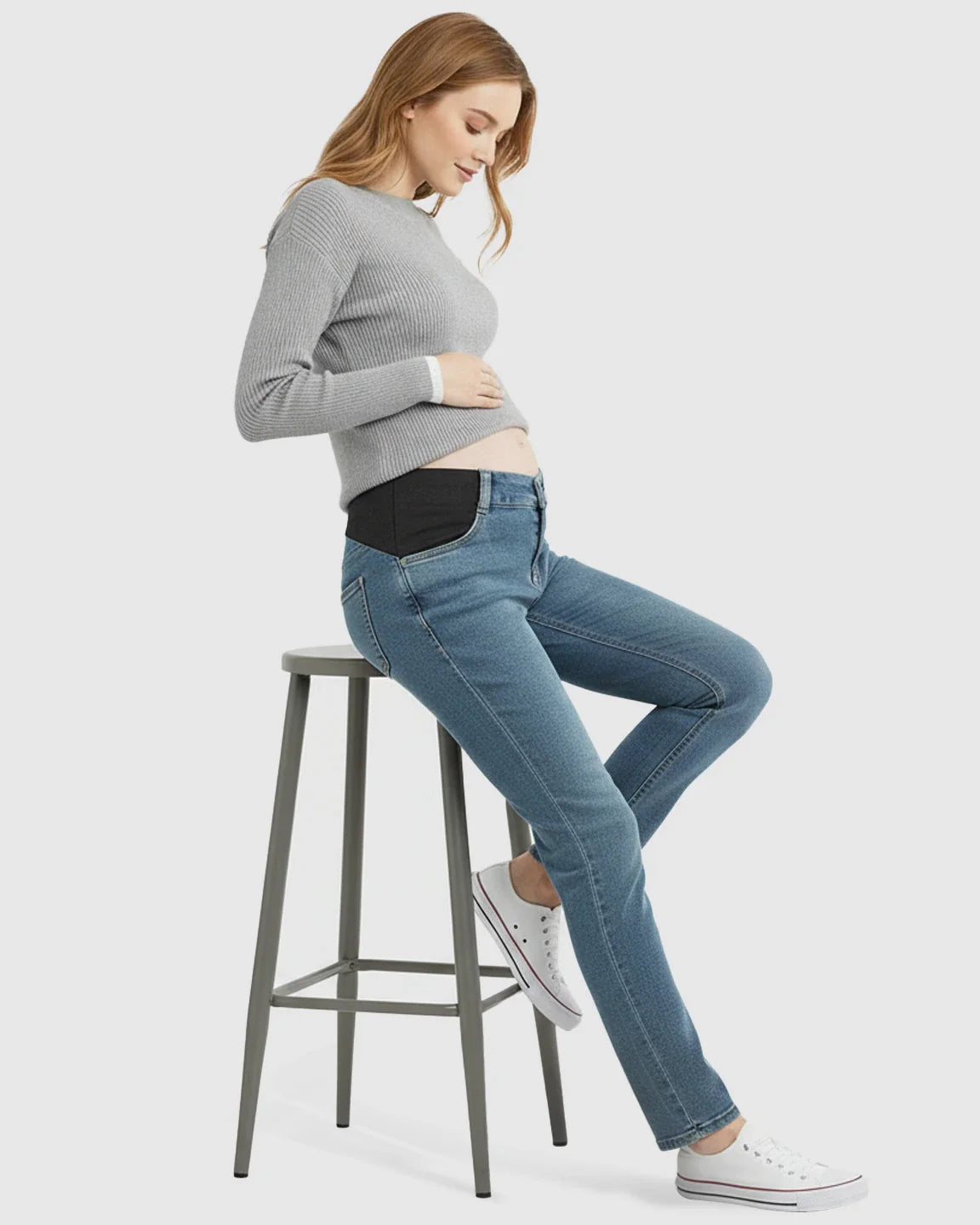 Woman in light wash straight-leg maternity jeans with black side panels, gray ribbed sweater, and white sneakers.