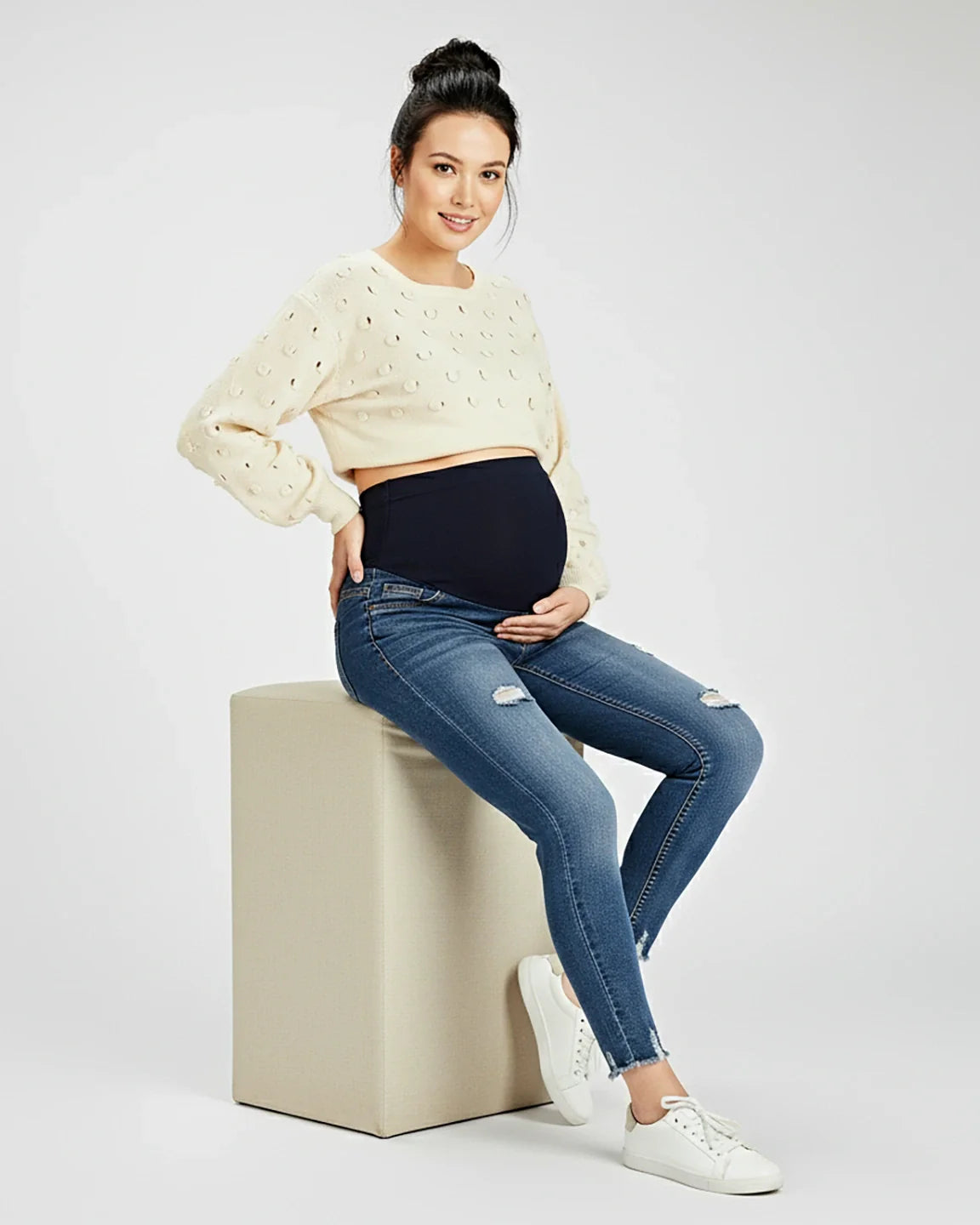 Smiling pregnant woman in blue distressed skinny maternity jeans with a black elastic waistband.