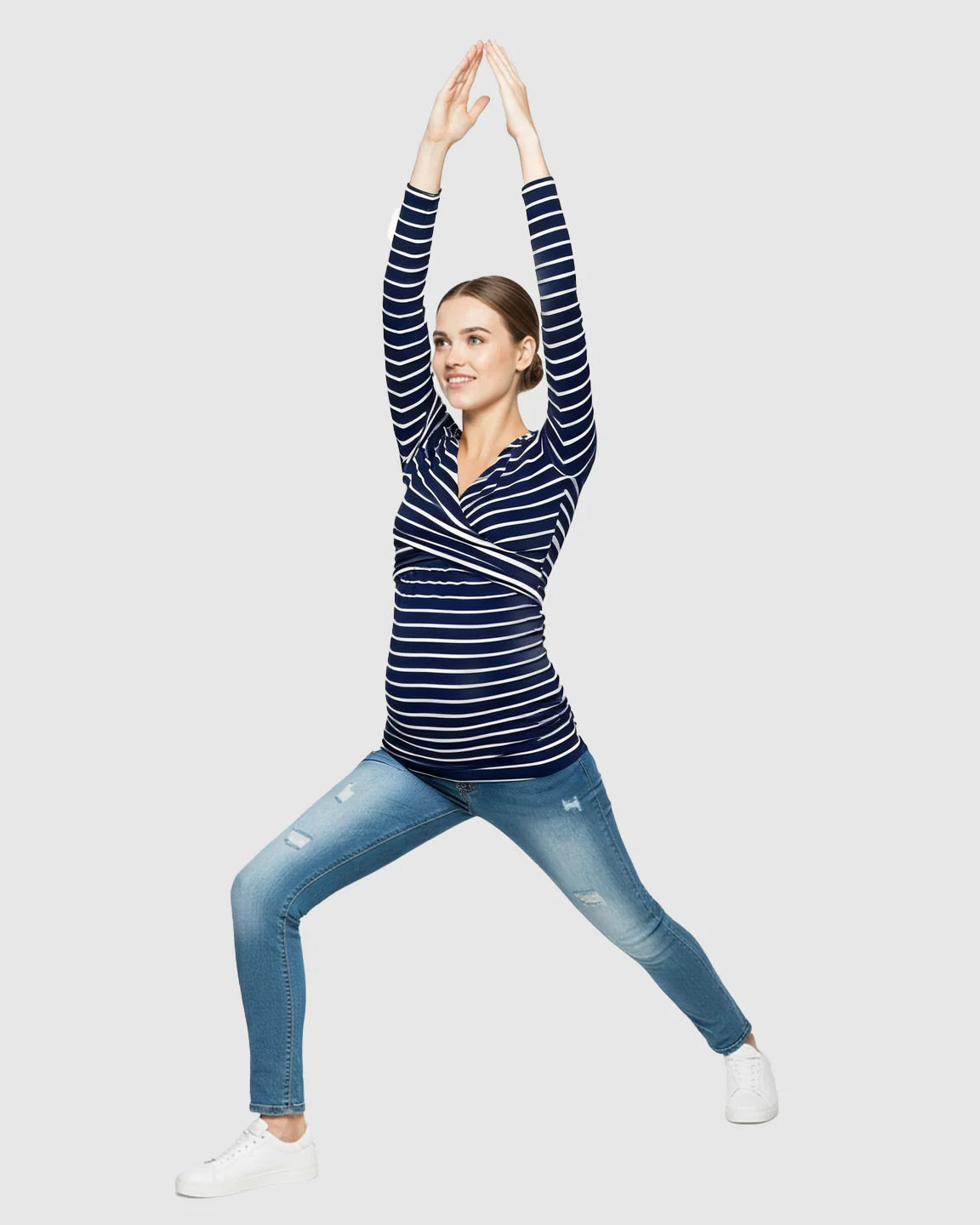 Pregnant woman in a navy and white striped long-sleeve V-neck wrap maternity and nursing shirt, arms raised.