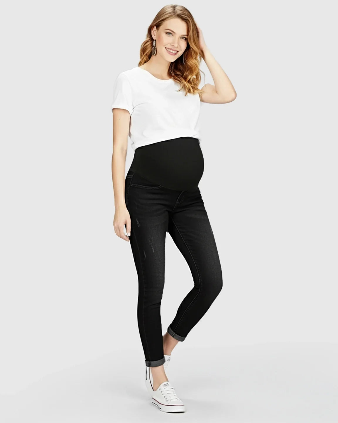 Smiling pregnant woman in black distressed maternity skinny jeans with full panel and white t-shirt.