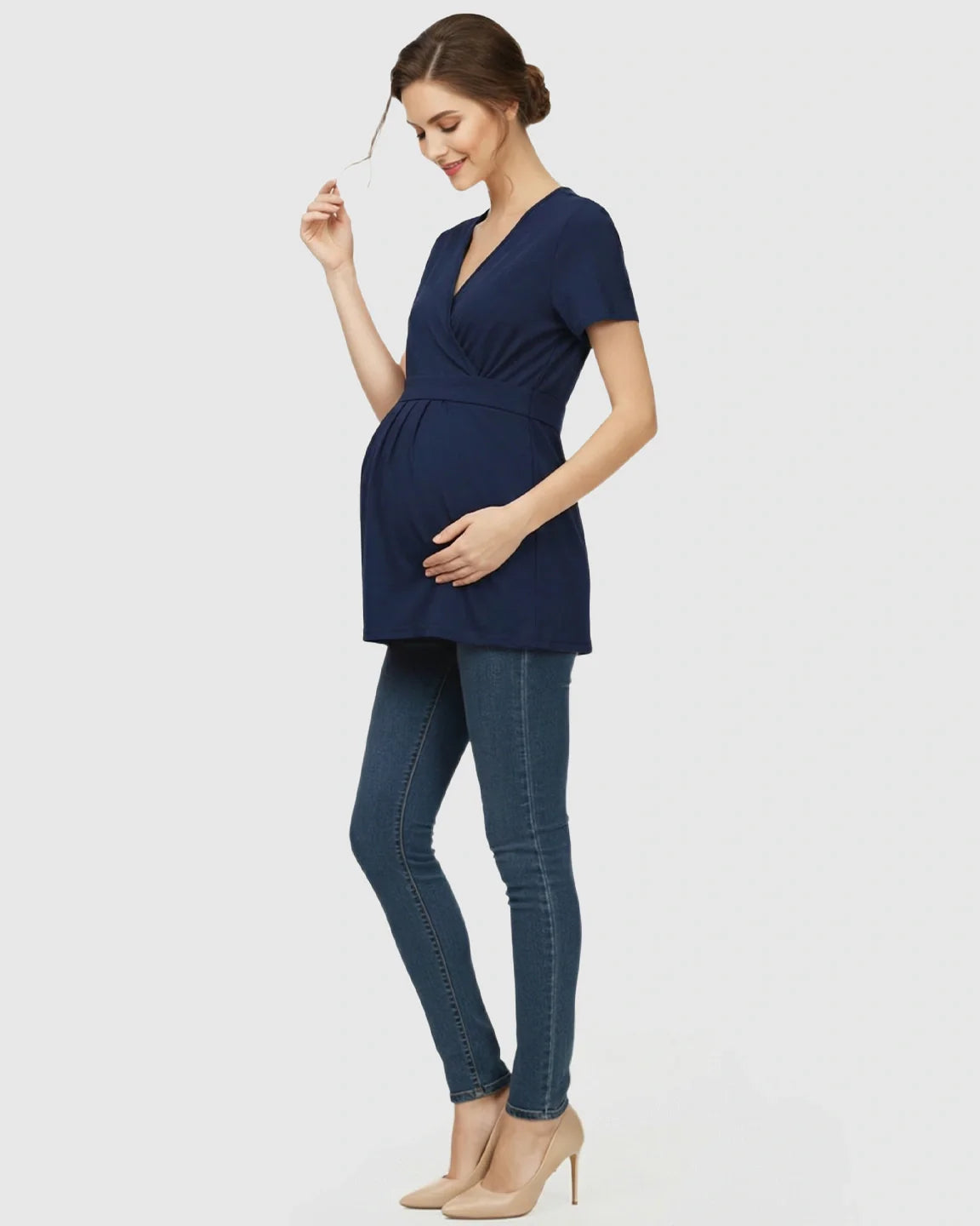 Woman in navy V-neck wrap-style maternity top with adjustable waist tie, paired with jeans and heels.