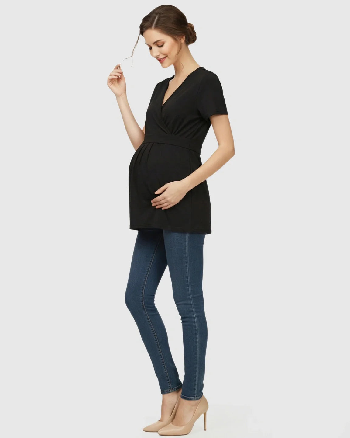 Woman in black V-neck wrap-style maternity top with short sleeves, adjustable waist tie, and blue jeans.