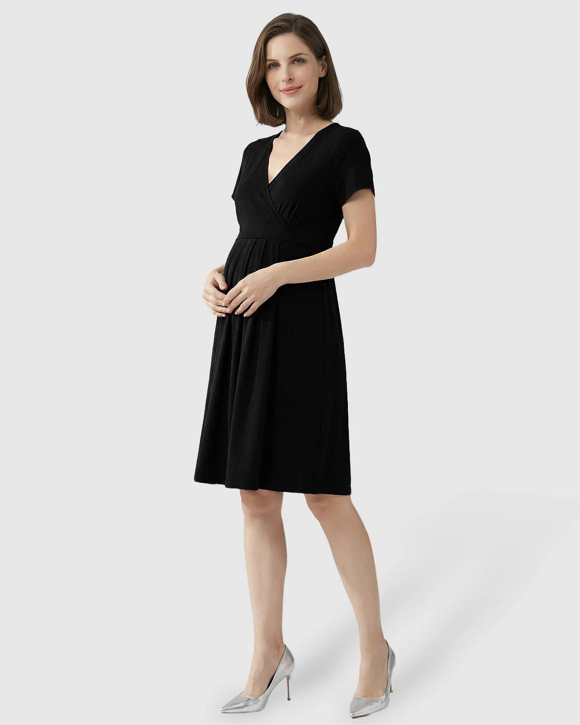 Woman in a black V-neck A-line maternity and nursing dress with short sleeves, posing in silver heels.