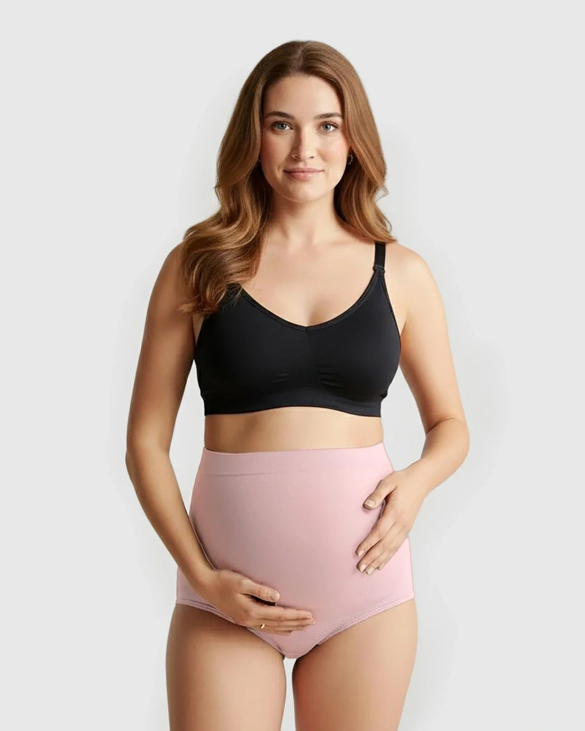 Smiling pregnant woman models pink high-waist seamless maternity panties and a black bra.