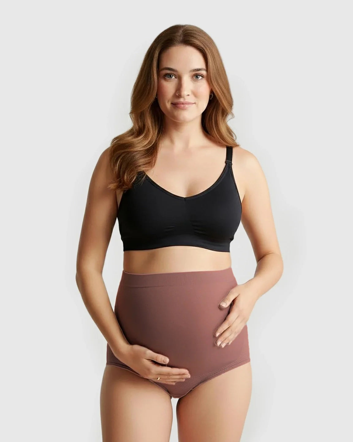 Pregnant woman wearing Bump Society's high-waist seamless maternity panties in dusty rose, with a black bra.