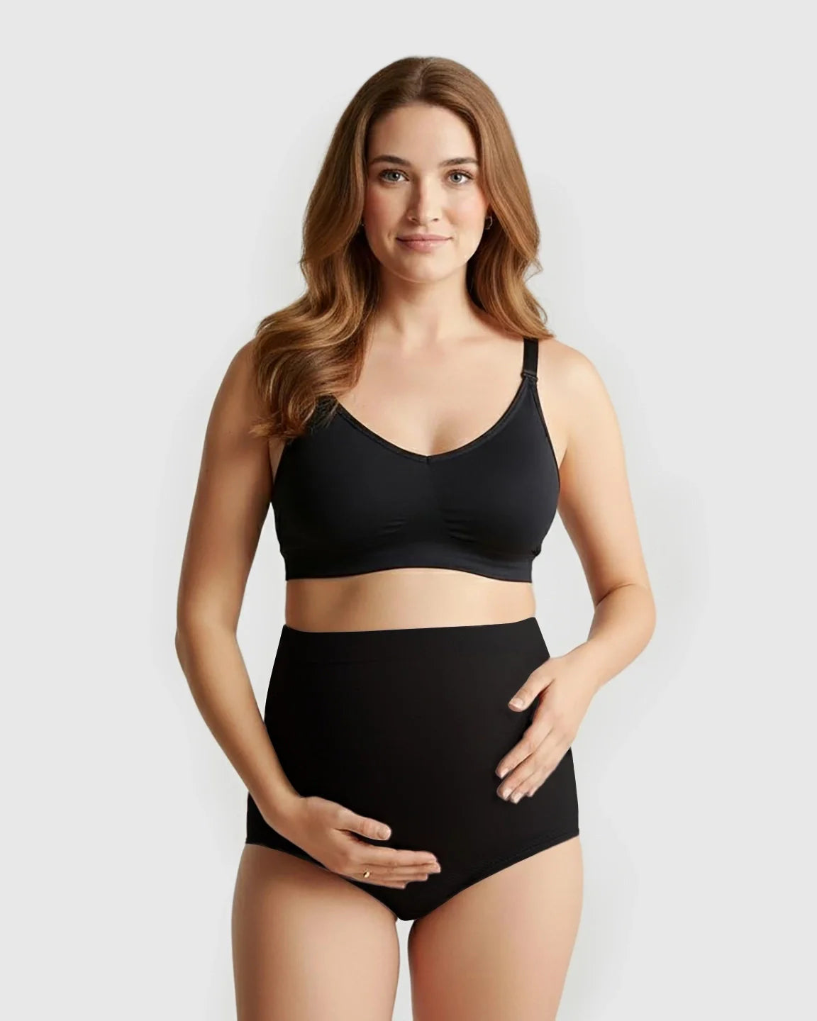 Pregnant woman in black seamless high-waist maternity panties and matching bra, cradling her bump.
