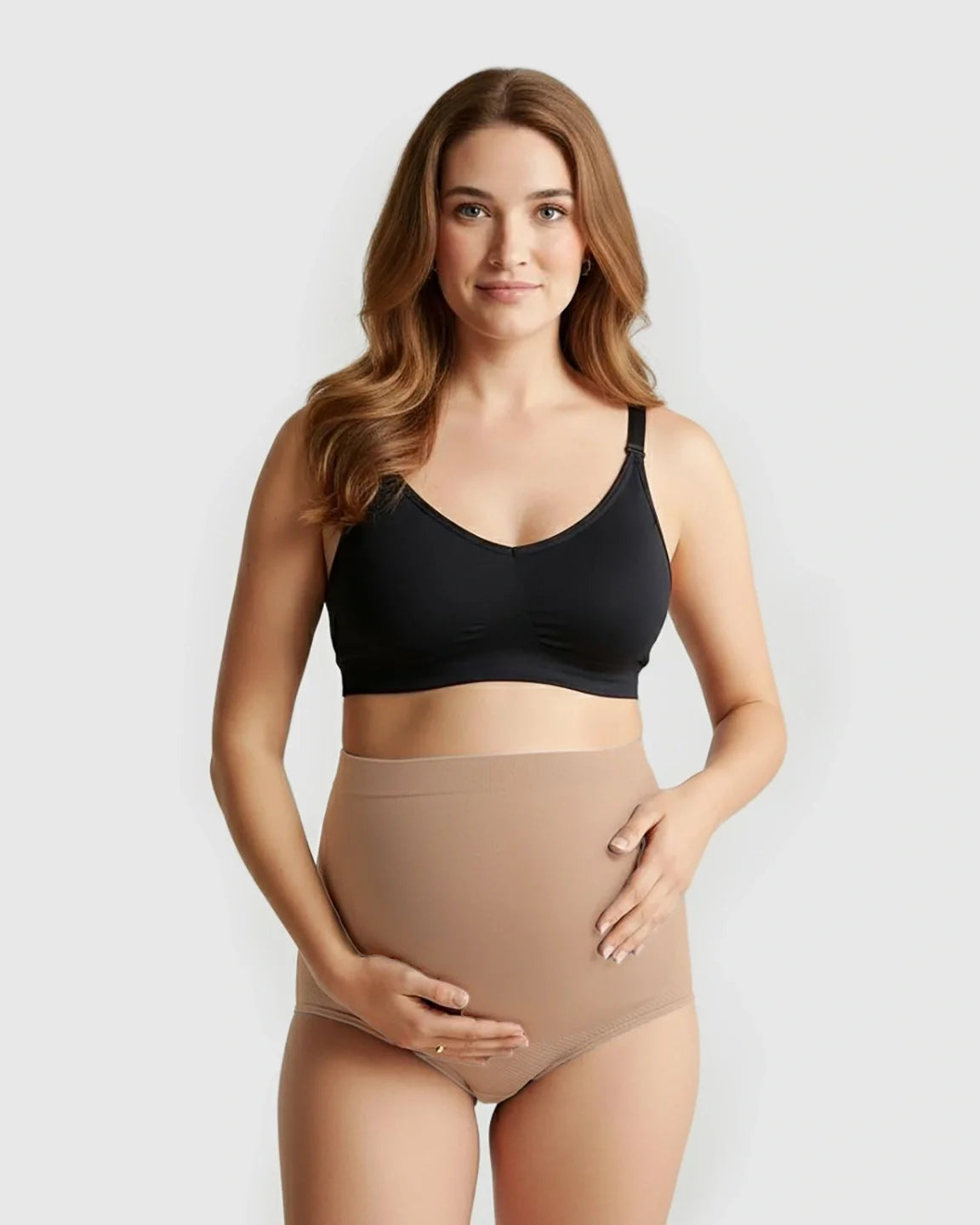 Woman wearing a black maternity bra and seamless high-waist nude maternity panties, cradling her bump.