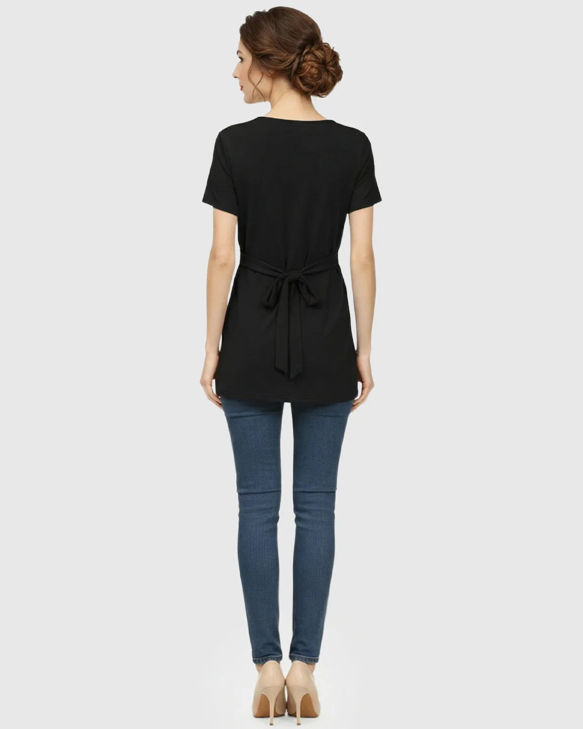 Back view of a woman wearing a black short-sleeve maternity top with a tied waist and blue jeans.