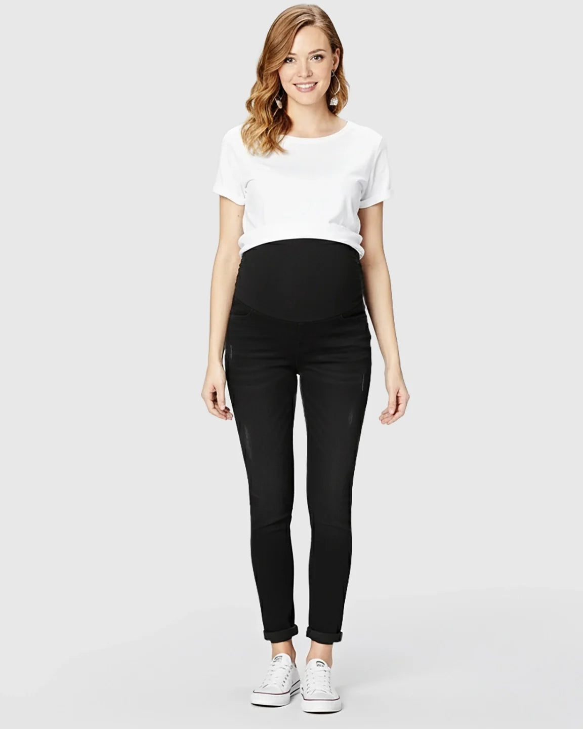 Smiling pregnant woman in black full panel distressed maternity skinny jeans and a white t-shirt.