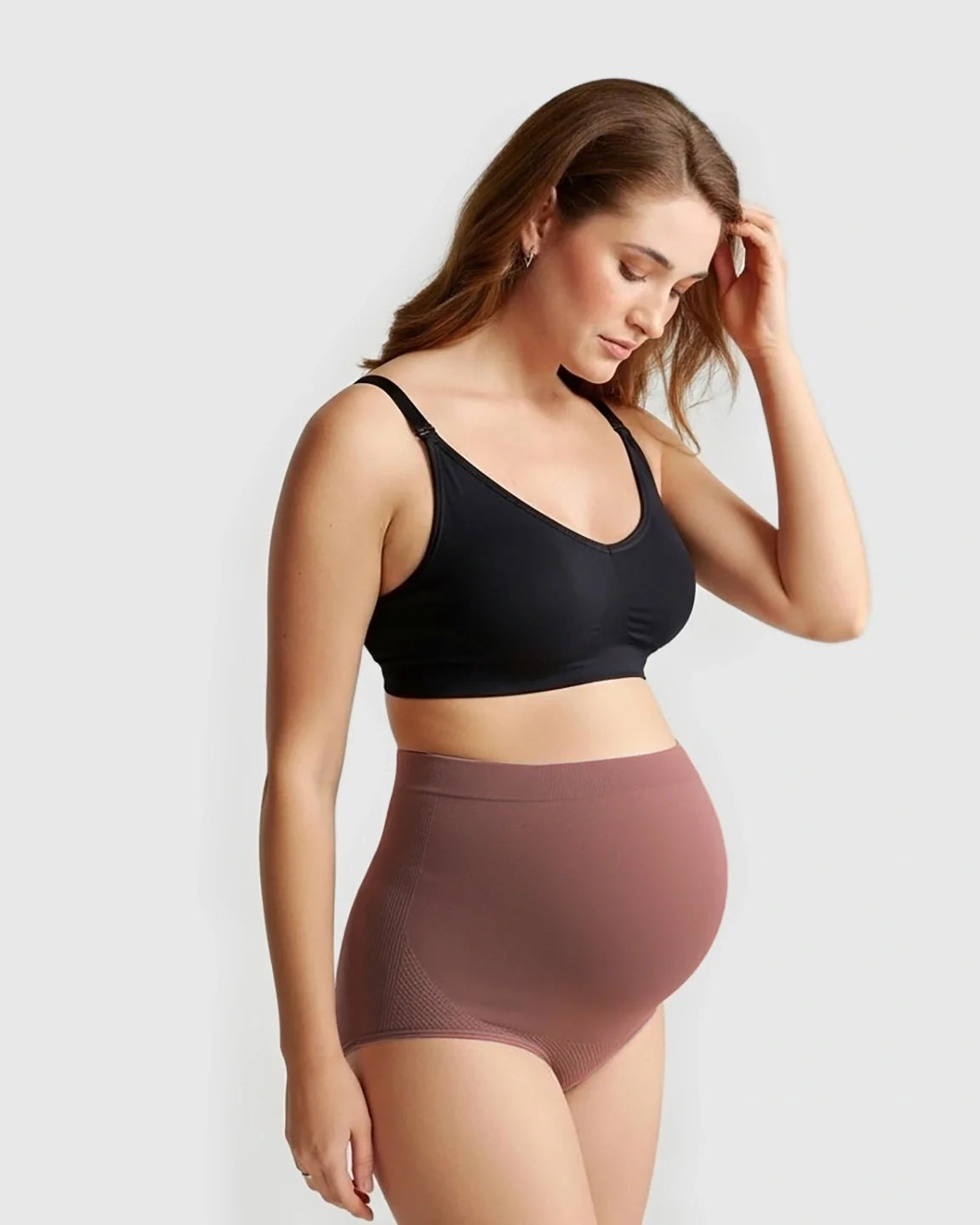 Pregnant woman wearing Bump Society's seamless high-waist maternity panties in dusty rose and a black bra.