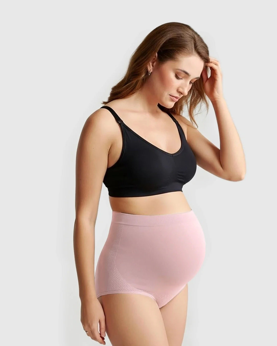 Pregnant woman wearing pink high-waist seamless maternity panties and a black bra.