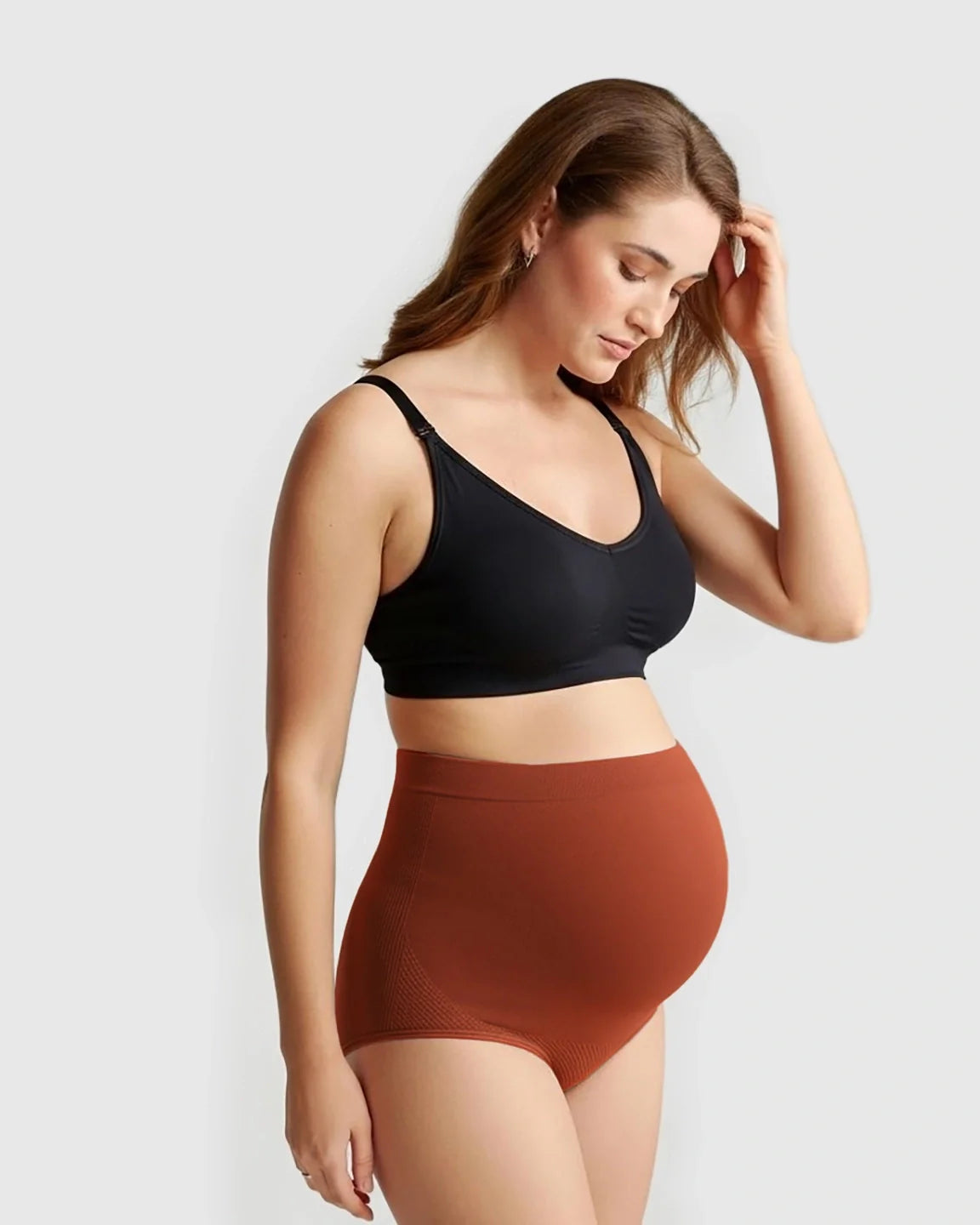 Pregnant woman in a black maternity bra and rust-colored seamless high-waist maternity panties.